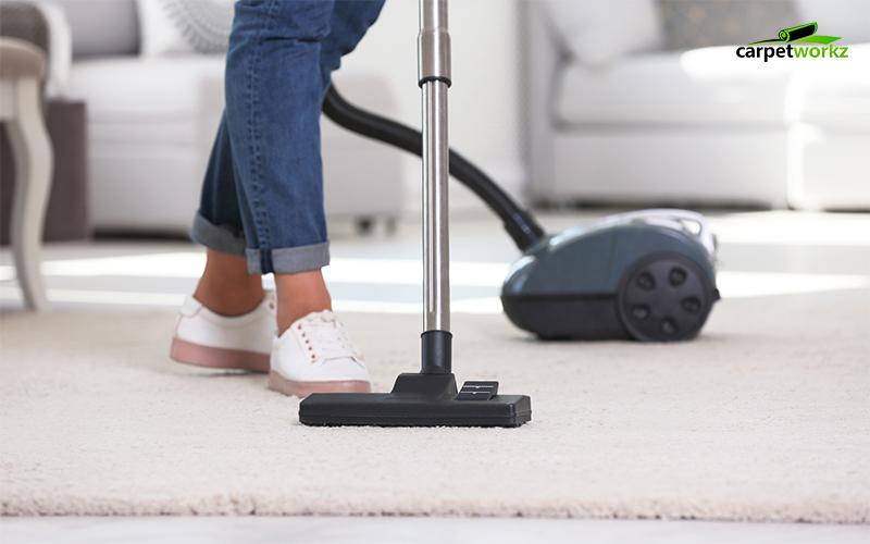 A person cleaning the carpet using a vacuum cleaner.